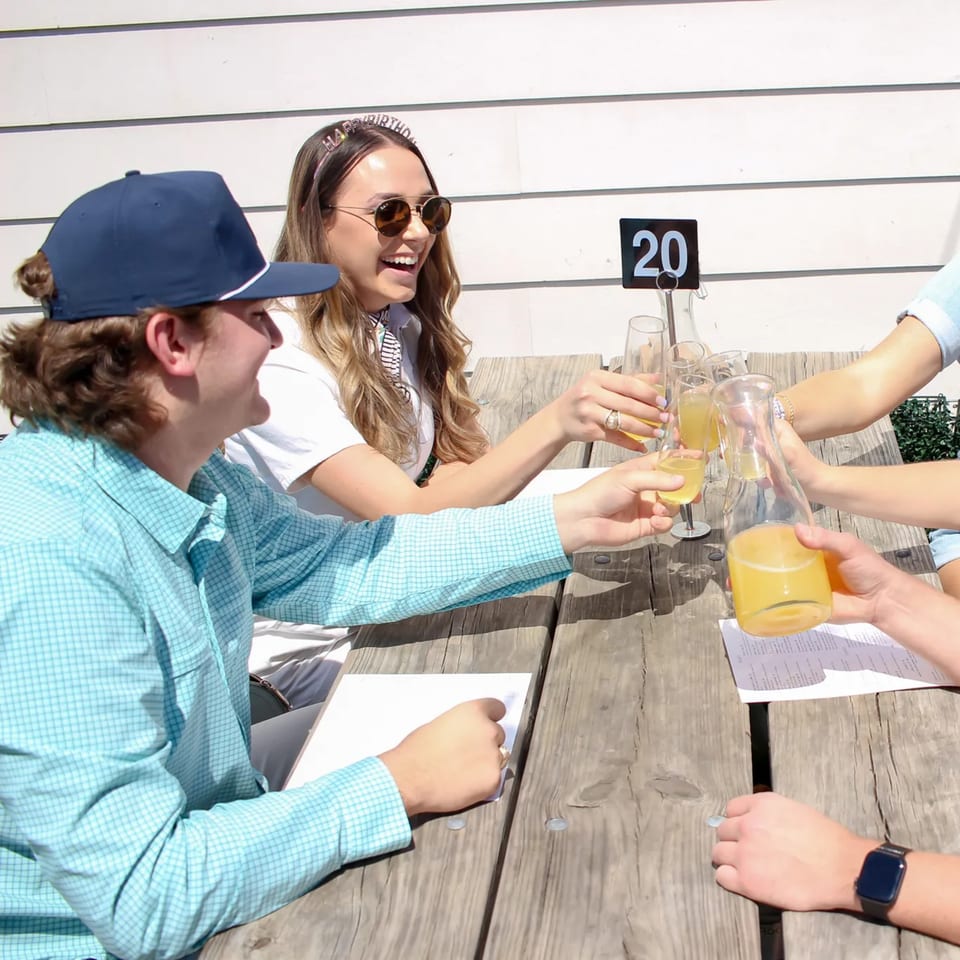 Friends celebrating a birthday at Bungalow Heights, toasting mimosas at an outdoor wooden table.