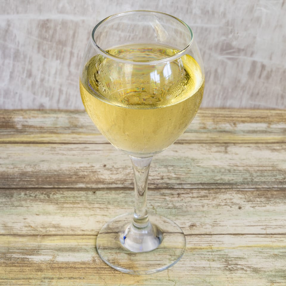 A glass of chilled white wine sits on a rustic wooden table at Bungalow Heights.