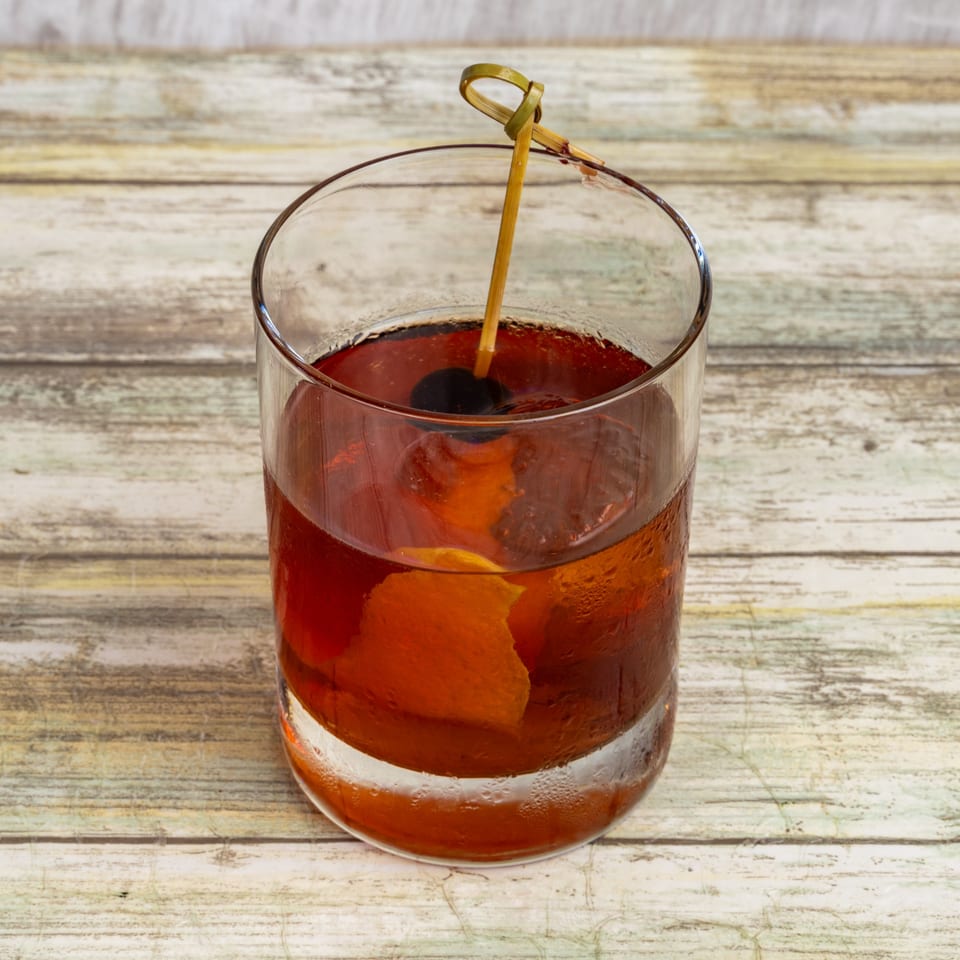 A Bungalow Heights Old Fashioned cocktail with a cherry and orange peel on a wooden table.