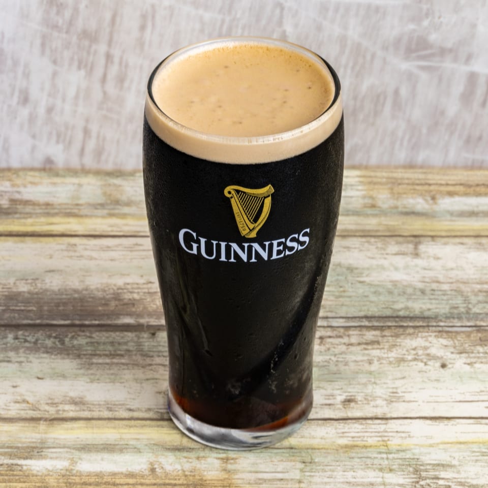 A cold pint of Guinness stout with a creamy head on a rustic wooden table.