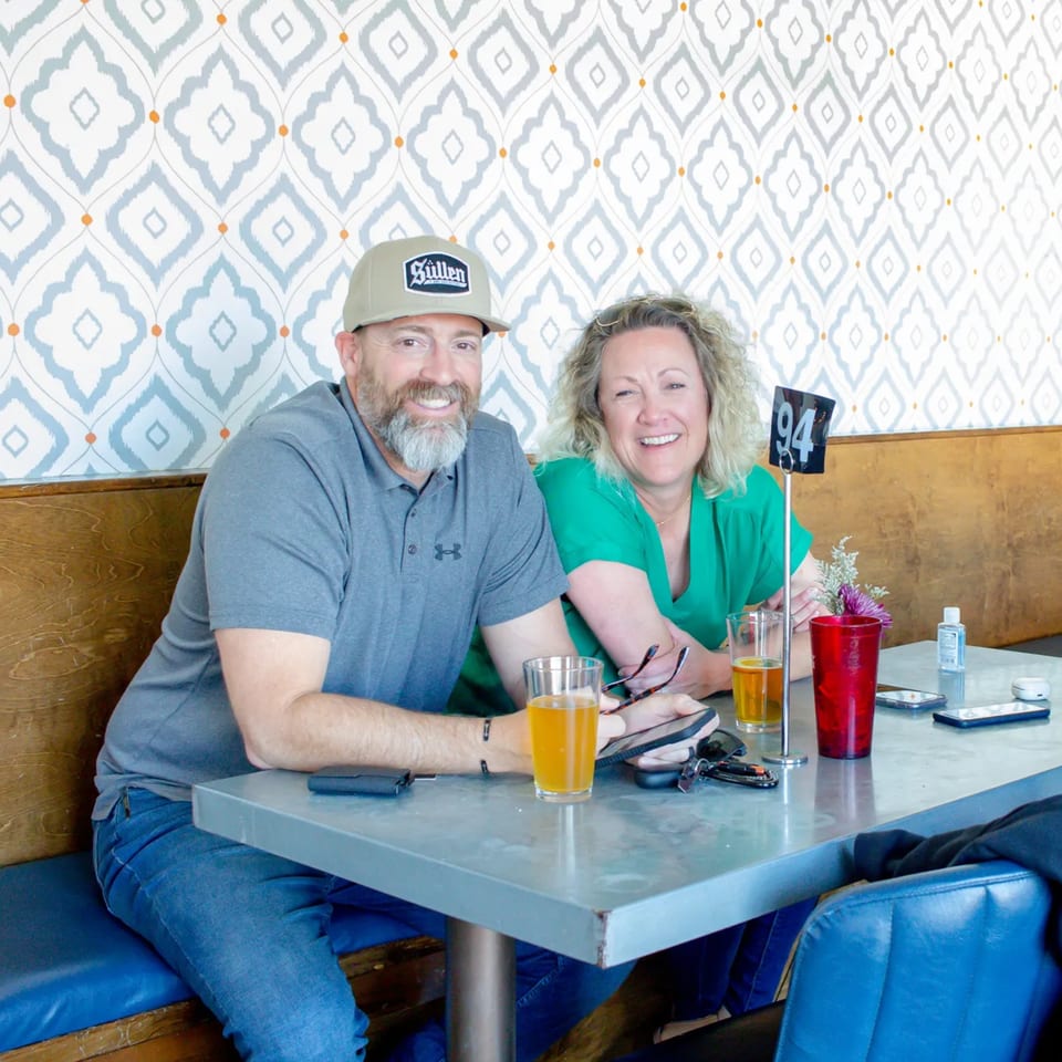 A smiling man and woman sit at a table with drinks at Bungalow Heights bar-and-grill.