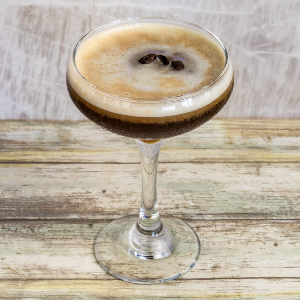 Espresso martini with foam and three coffee beans on a rustic wooden table at Bungalow Heights.