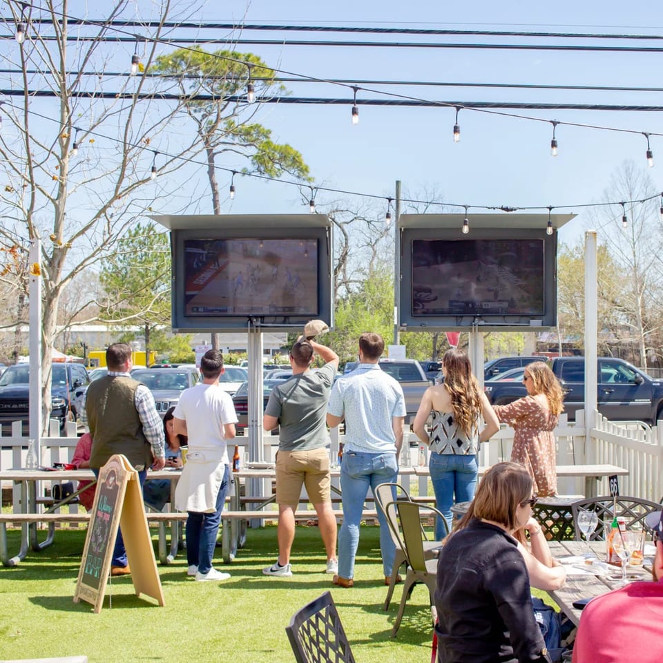 Patrons at Bungalow Heights' outdoor bar-and-grill patio watch sports on large screens.