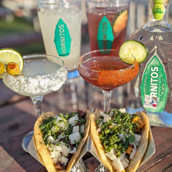 Two tacos and four Hornitos cocktails, including margaritas and other mixed drinks, on a wooden table.