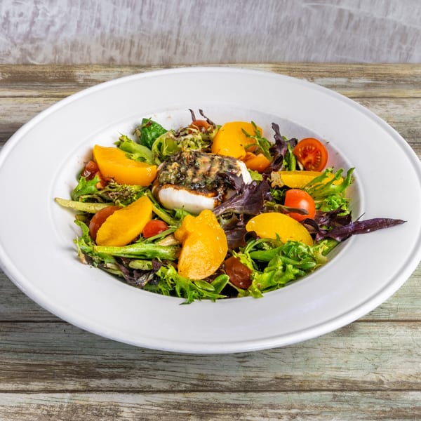 A fresh salad with mixed greens, sliced peaches, cherry tomatoes, and a burrata cheese ball.
