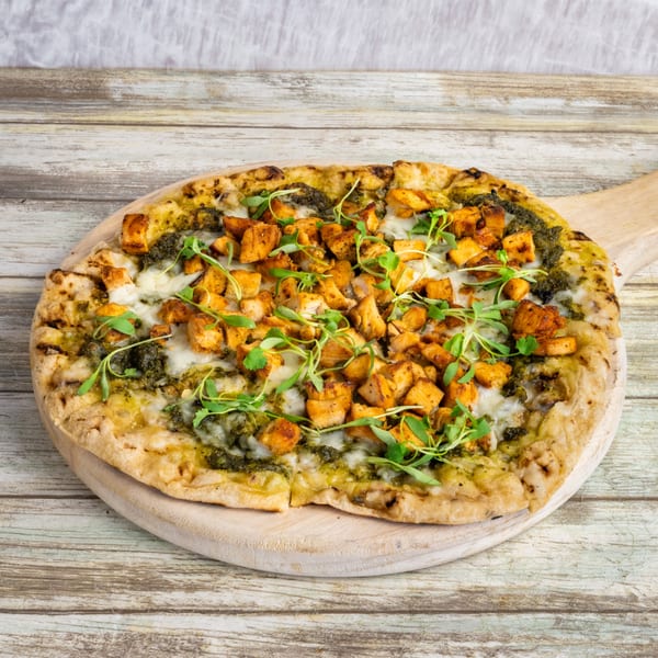 Bungalow Heights' pesto chicken flatbread pizza with melted cheese and microgreens on a wooden board.