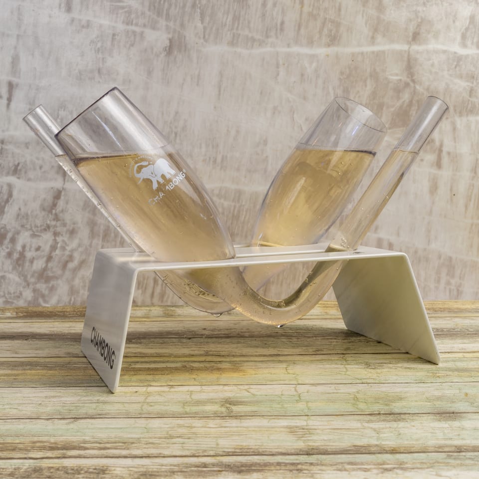 Two Chambong glasses filled with champagne, resting in a white stand on a wooden surface.