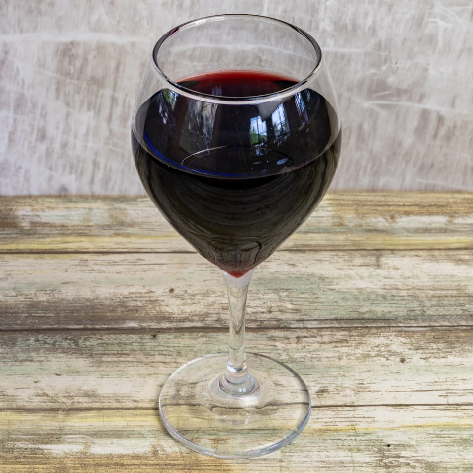 A glass of red wine sits on a rustic wooden table at Bungalow Heights.