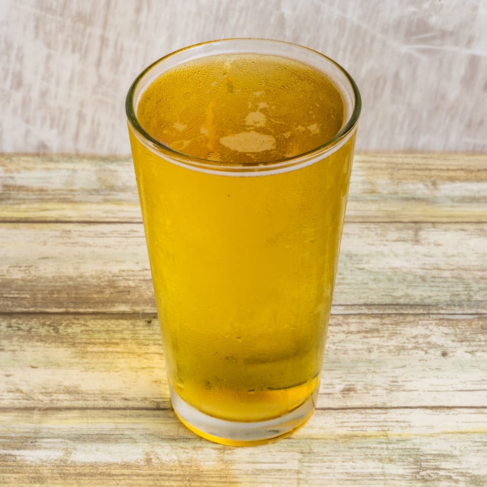 A cold, sweating glass of golden beer sits on a rustic wooden table at Bungalow Heights.