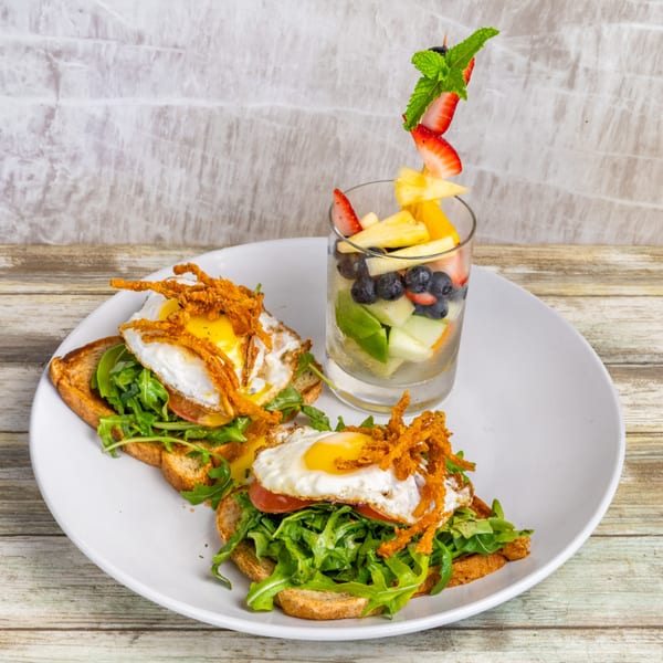 Two avocado toasts with fried eggs and crispy onions, served with a fruit cup.
